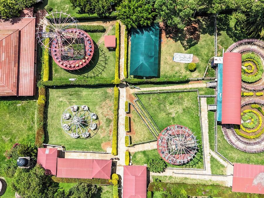 An aerial view of a park with a Ferris wheel, a carousel, and a circular garden with a red roof.