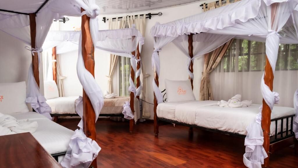 A room with four beds, each with a canopy. The room has wooden flooring and large windows.