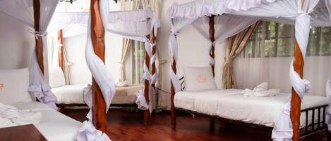 A room with four beds, each with a canopy. The room has wooden flooring and large windows.