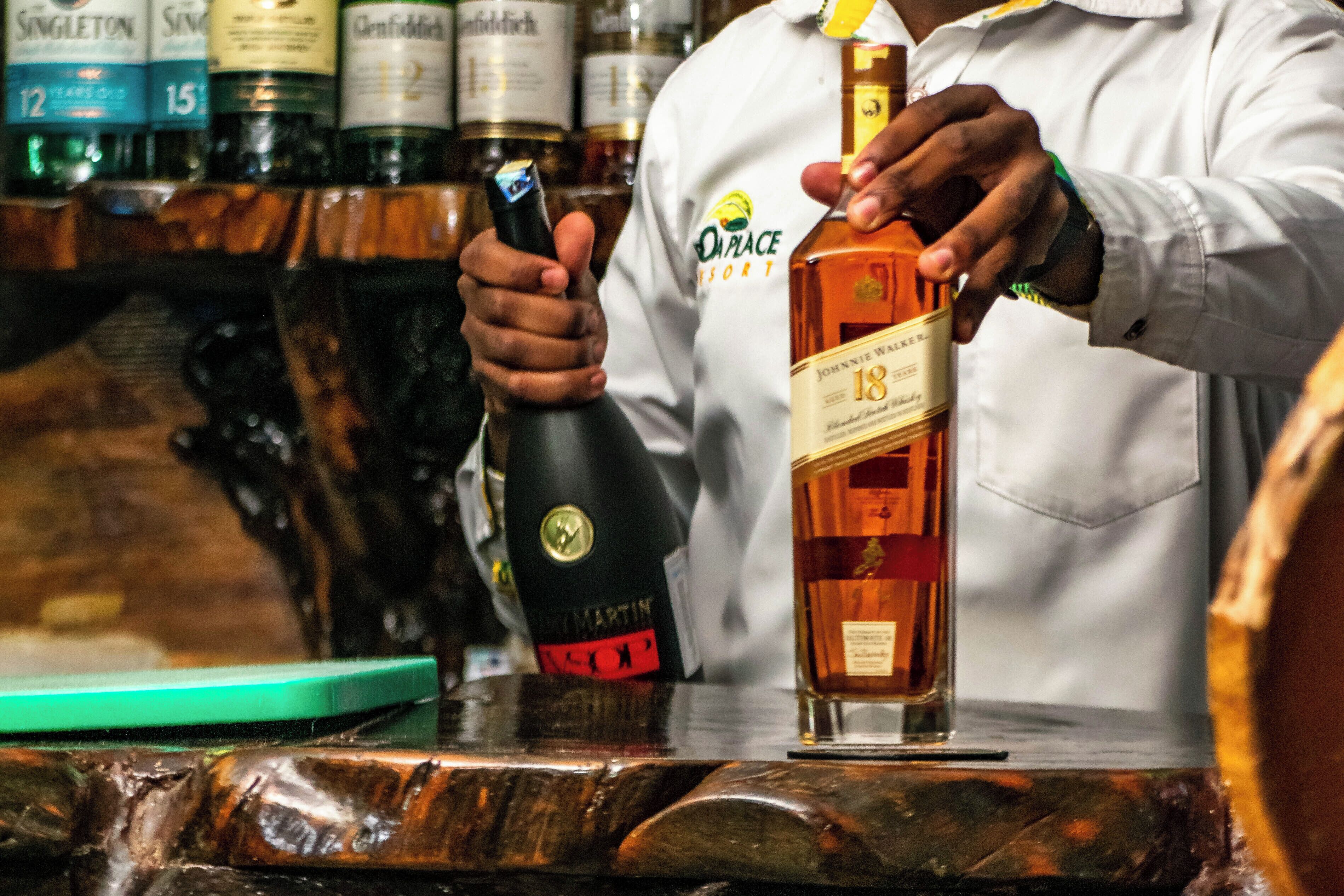 Un barman sirviendo una bebida desde una botella con la etiqueta 'Johnnie Walker 18' en un vaso.
