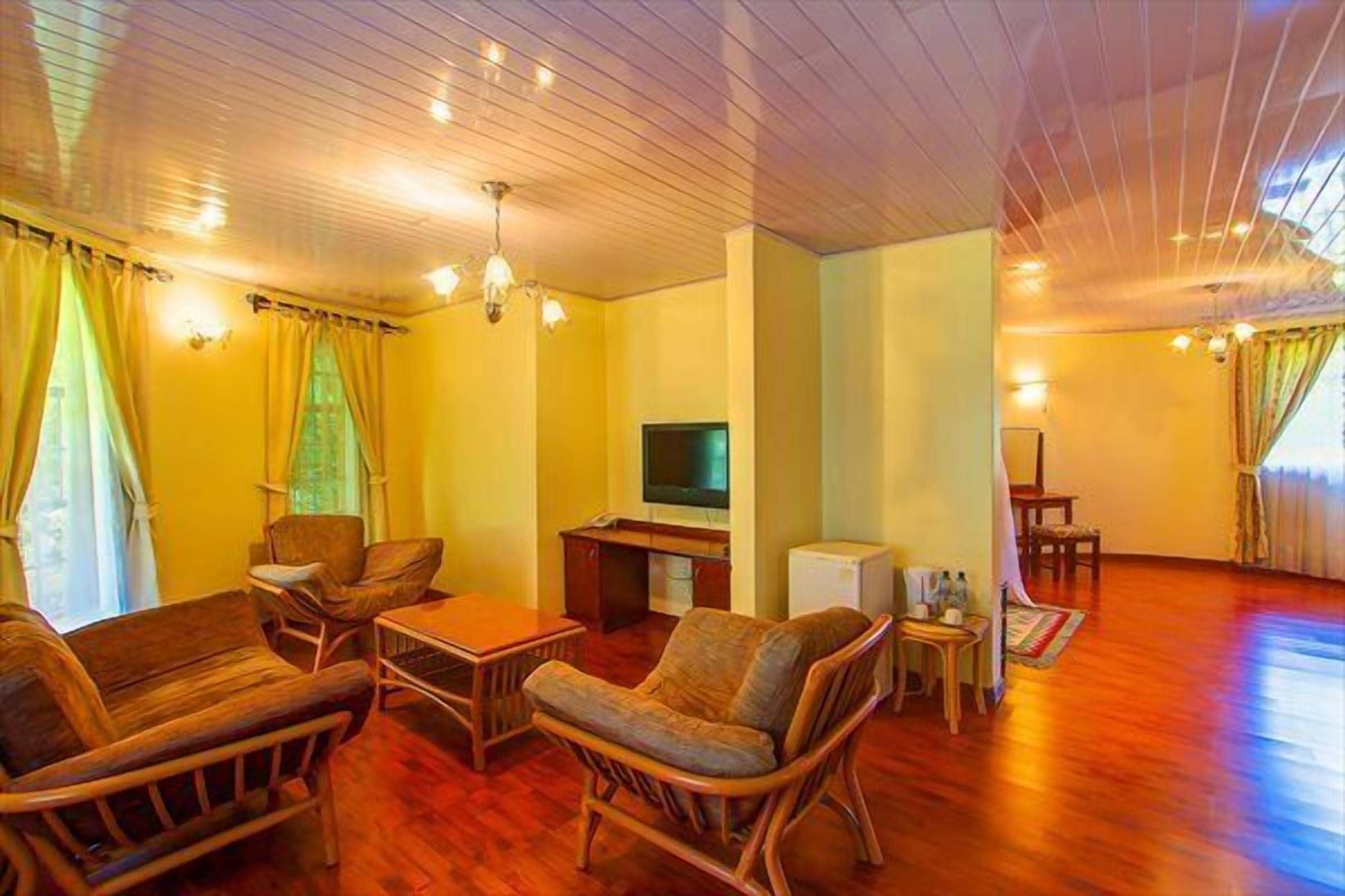 Amplia sala de estar con suelo de madera, televisor y un conjunto de asientos que incluye un sofá y sillones.