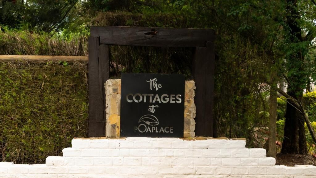 A sign for 'The Cottages at Poaplace' with a rustic wooden frame and white brick steps leading up to it.