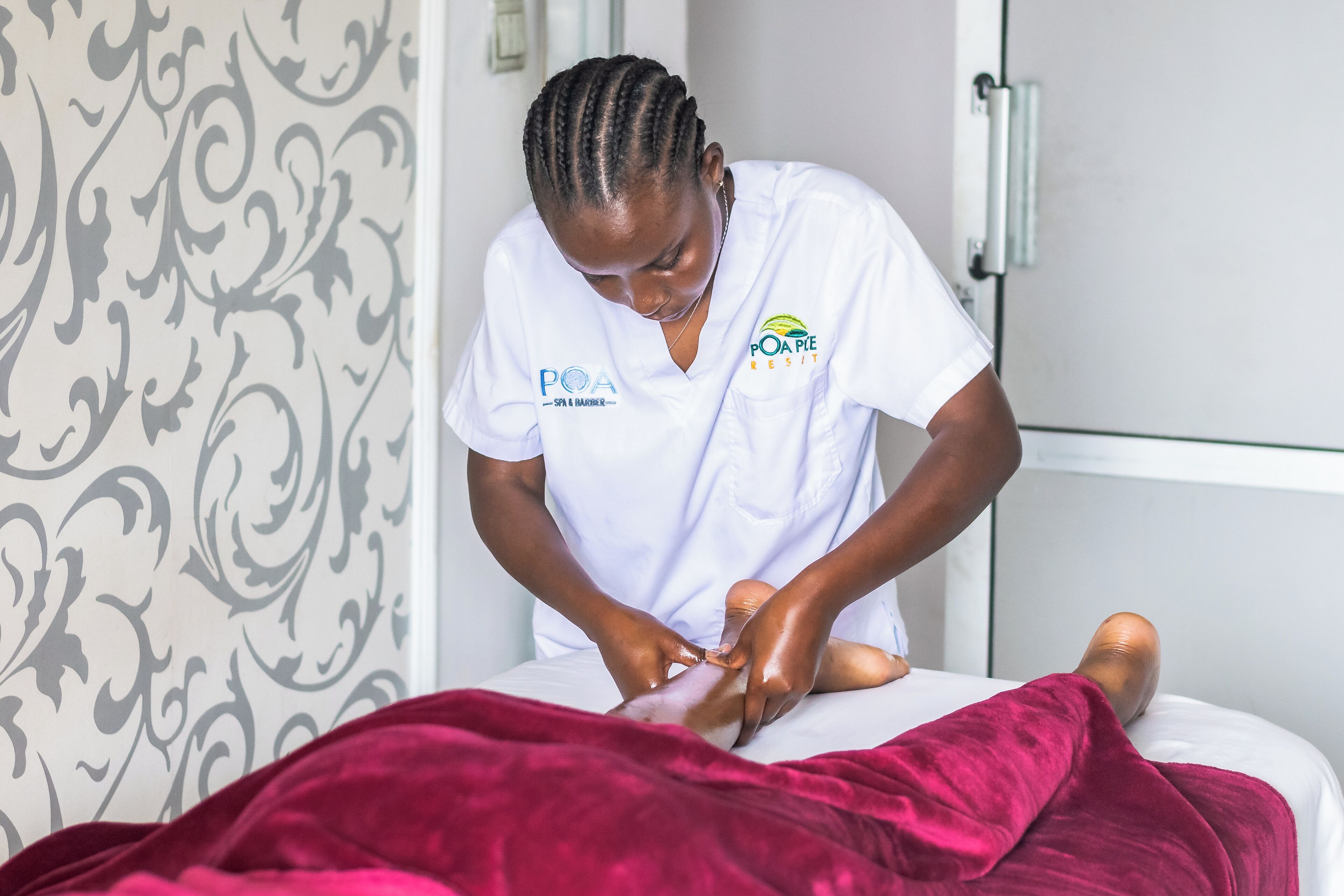 A person in a white uniform attending to a client on a bed with a red blanket.