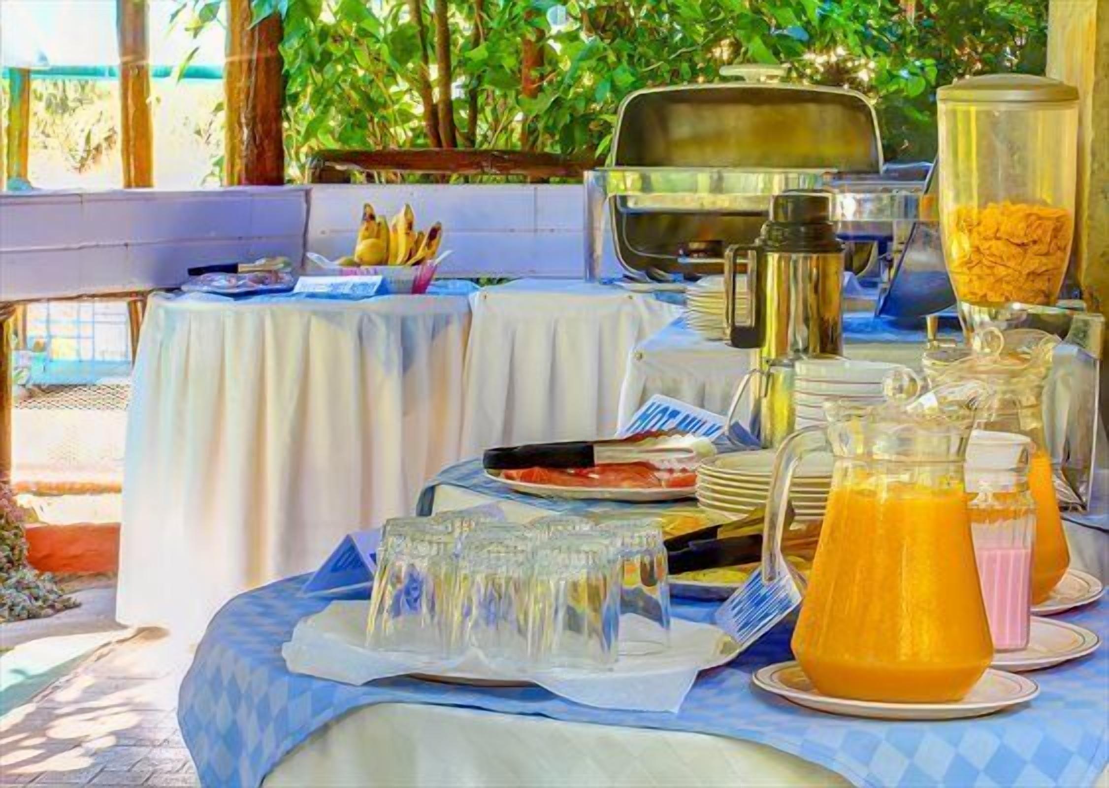 Buffet de café da manhã com diversas opções de alimentos, incluindo uma cesta de frutas, uma máquina de café e um dispensador de suco.