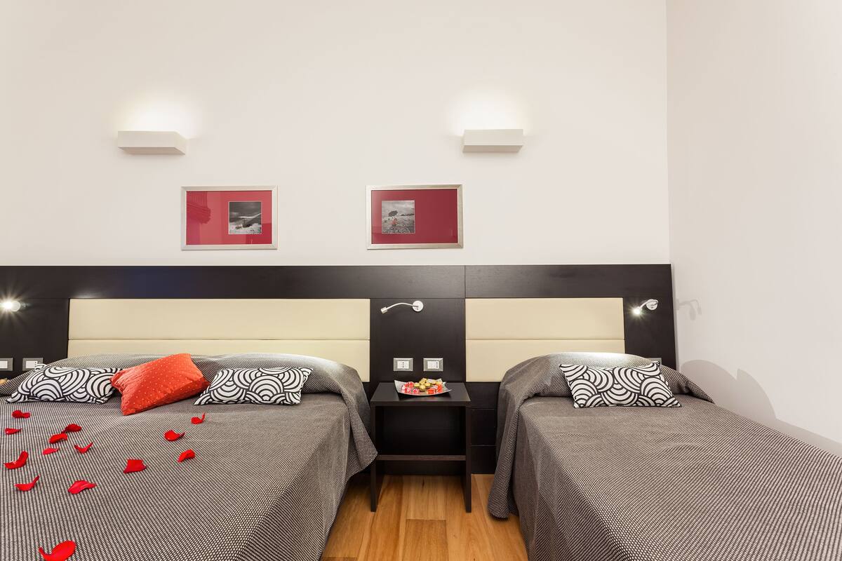 Una habitación de hotel con dos camas, una mesita de noche y dos lámparas fijadas a la pared.