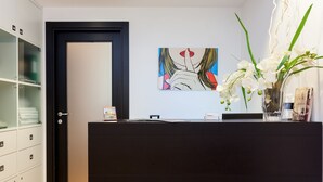 Zona de recepción con mostrador negro, vitrina con toallas dobladas, una obra de arte enmarco y un jarrón con orquídeas blancas.