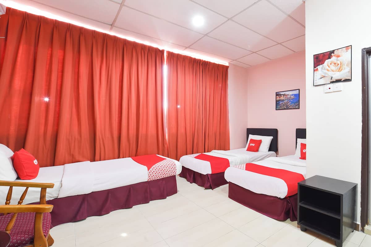 A hotel room with four beds, each with red and white bedding, a wooden chair, and a small black side table.