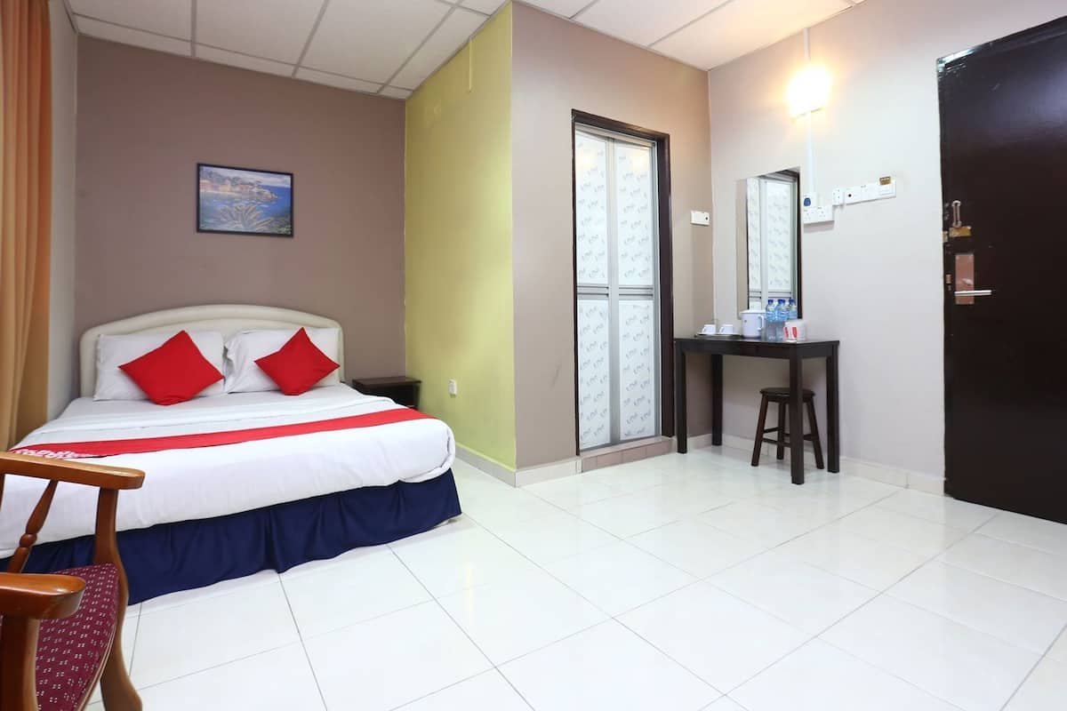 A hotel room with a bed, a desk, a chair, a window, and a door.