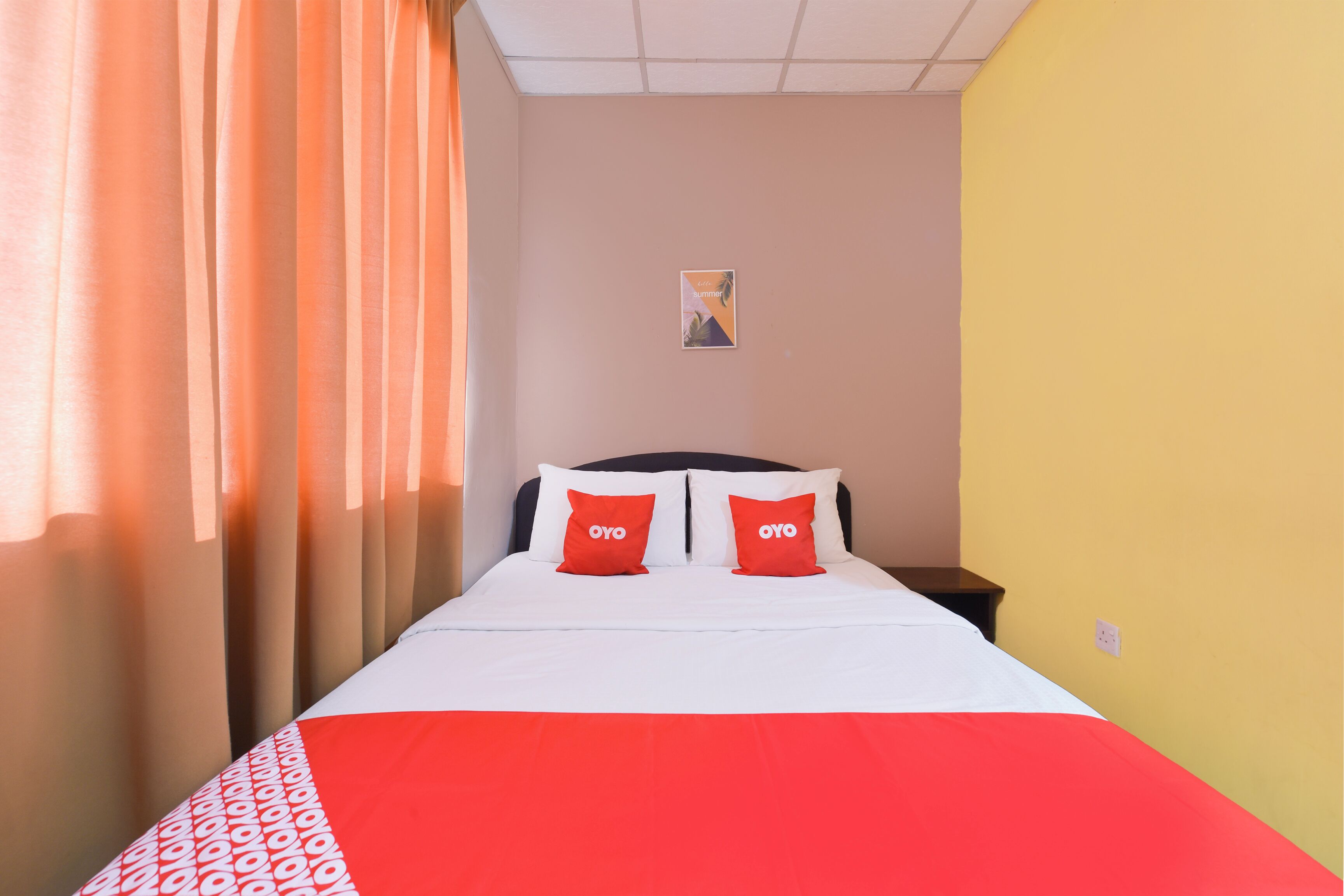 Una habitación de hotel con una cama, dos almohadas, una mesita de noche, un reloj de pared y un cartel en la pared.
