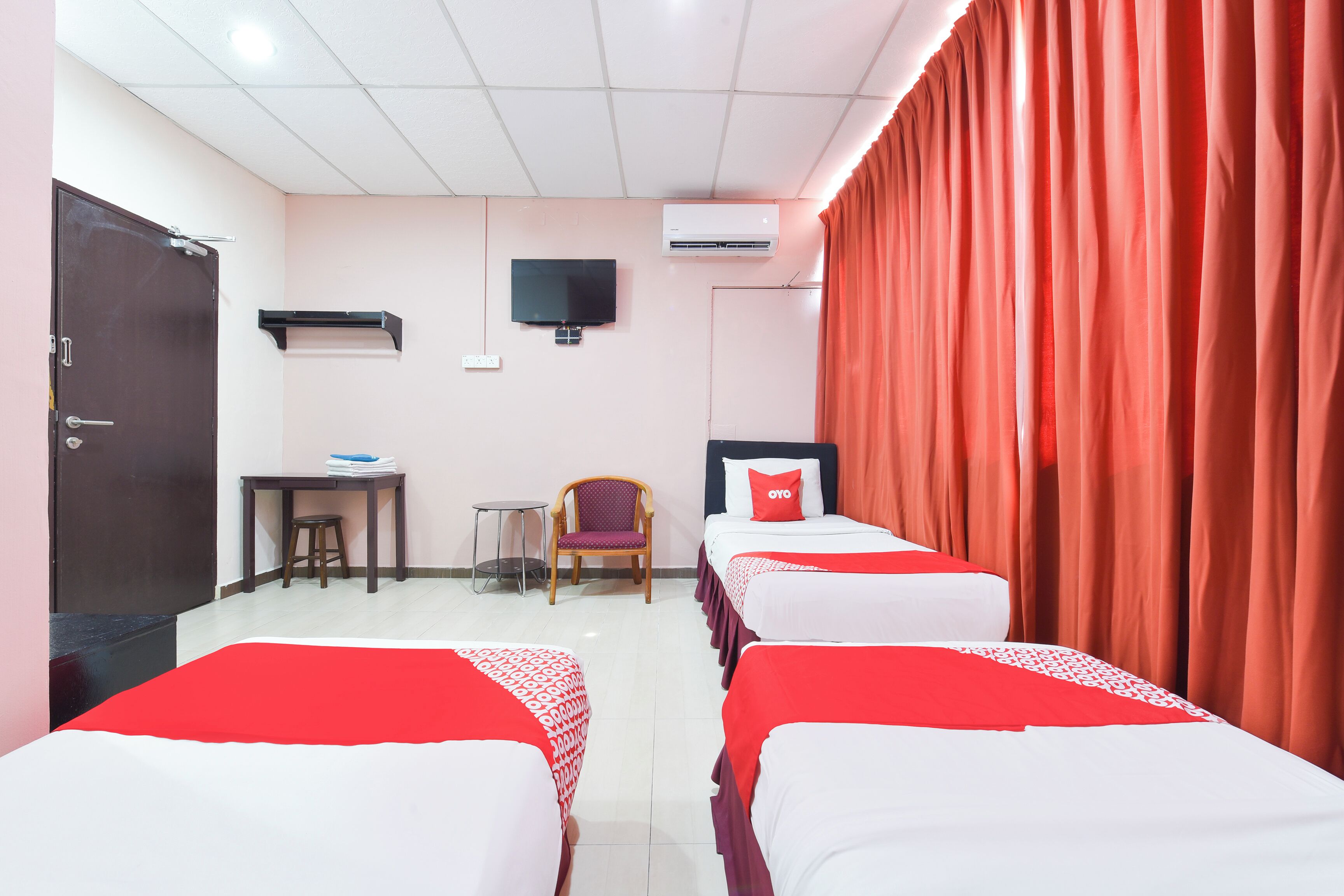 A hotel room with two beds, a desk, a chair, a TV, and an air conditioning unit.