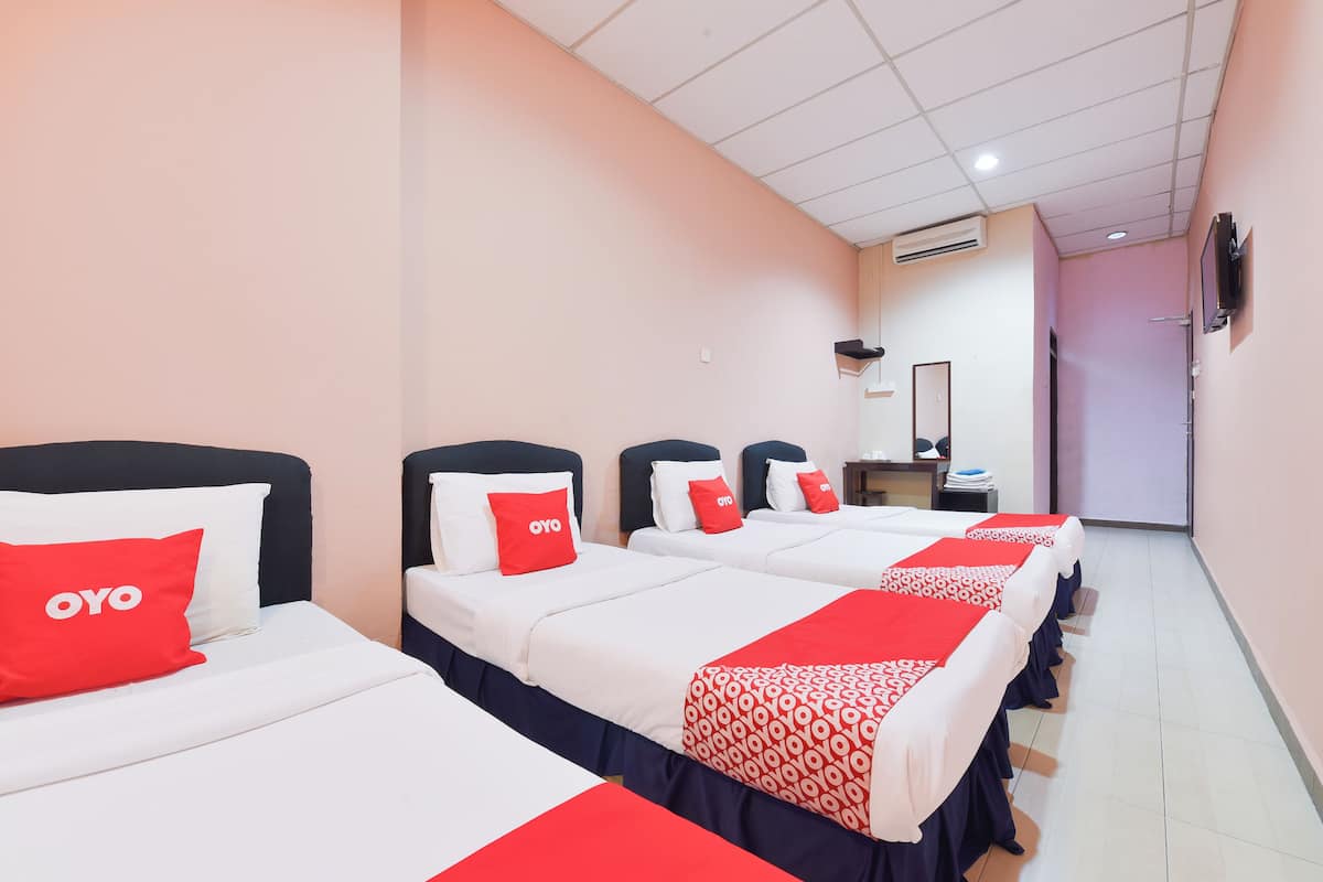 A hotel room with four beds, each with a red OYO branded pillow.
