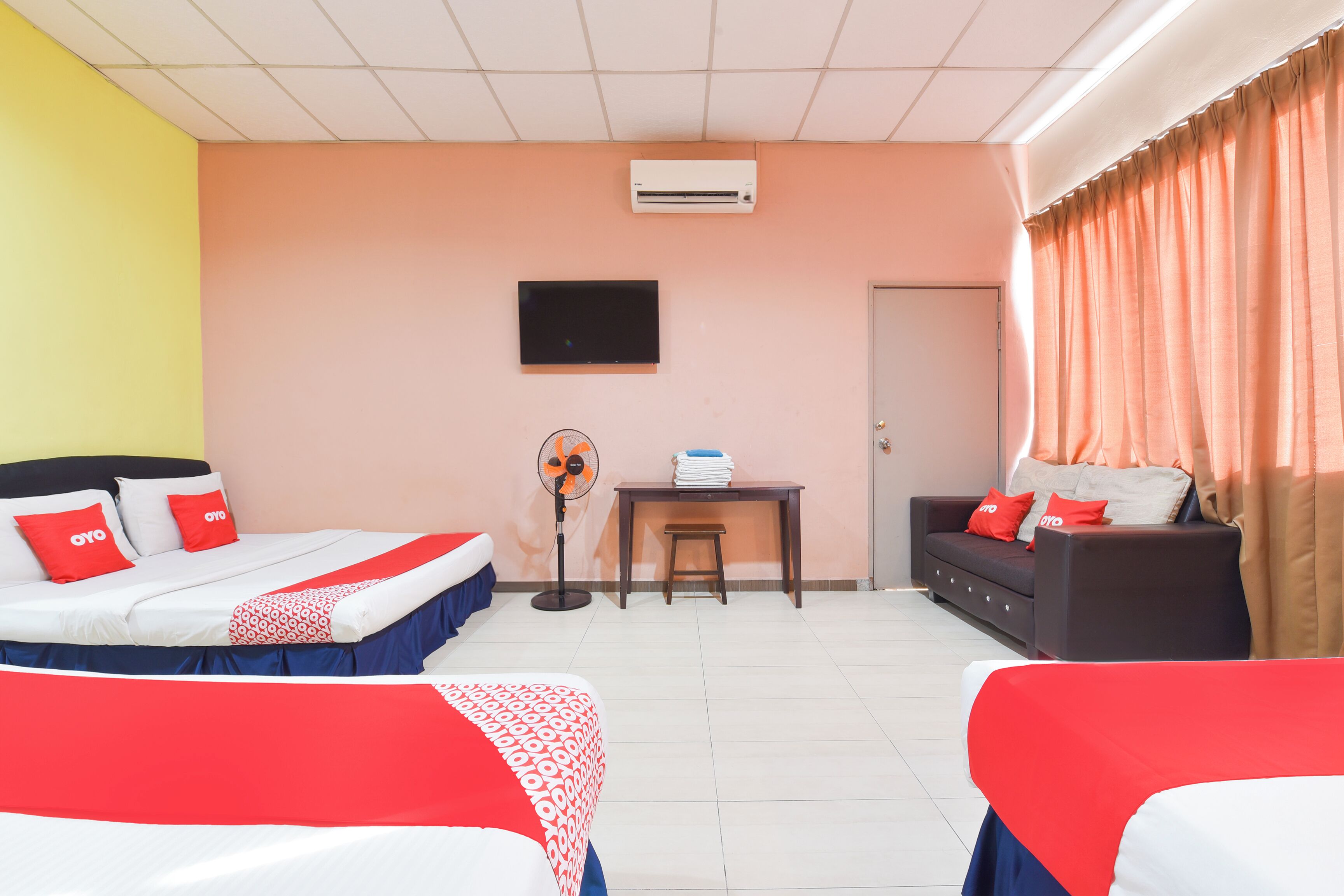 A hotel room with two beds, a desk, a chair, a TV, and a door.