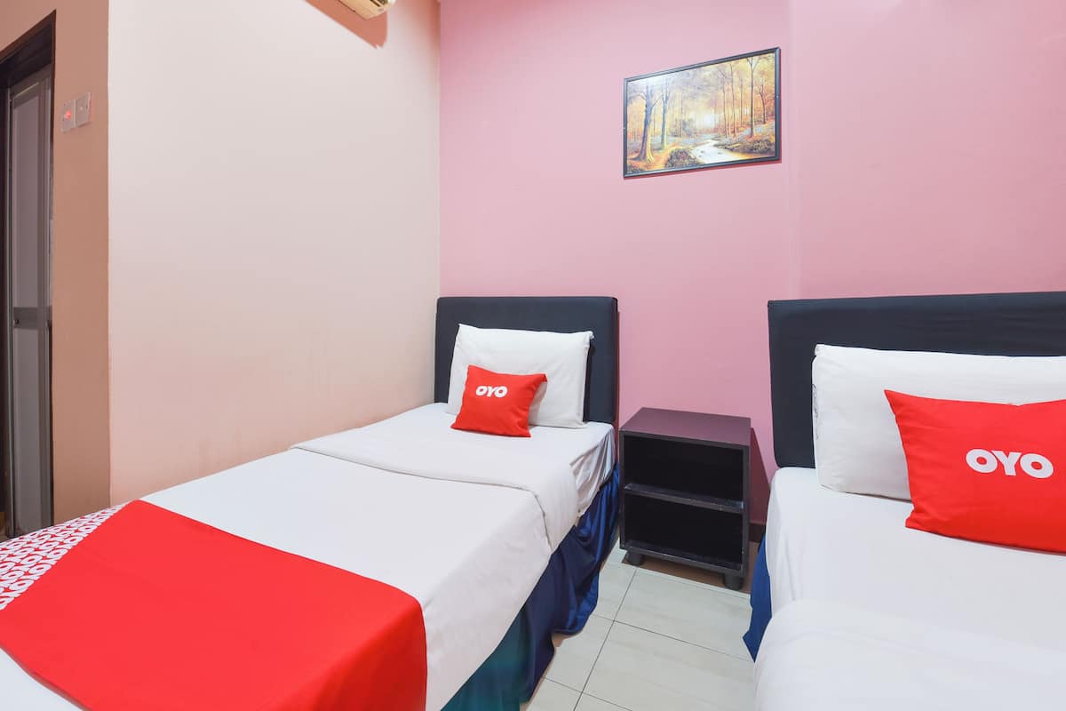 A hotel room with two beds, each with a white and red bedspread, and a red pillow with the brand 'OYO'. There is a painting on the wall and a small nightstand between the beds.