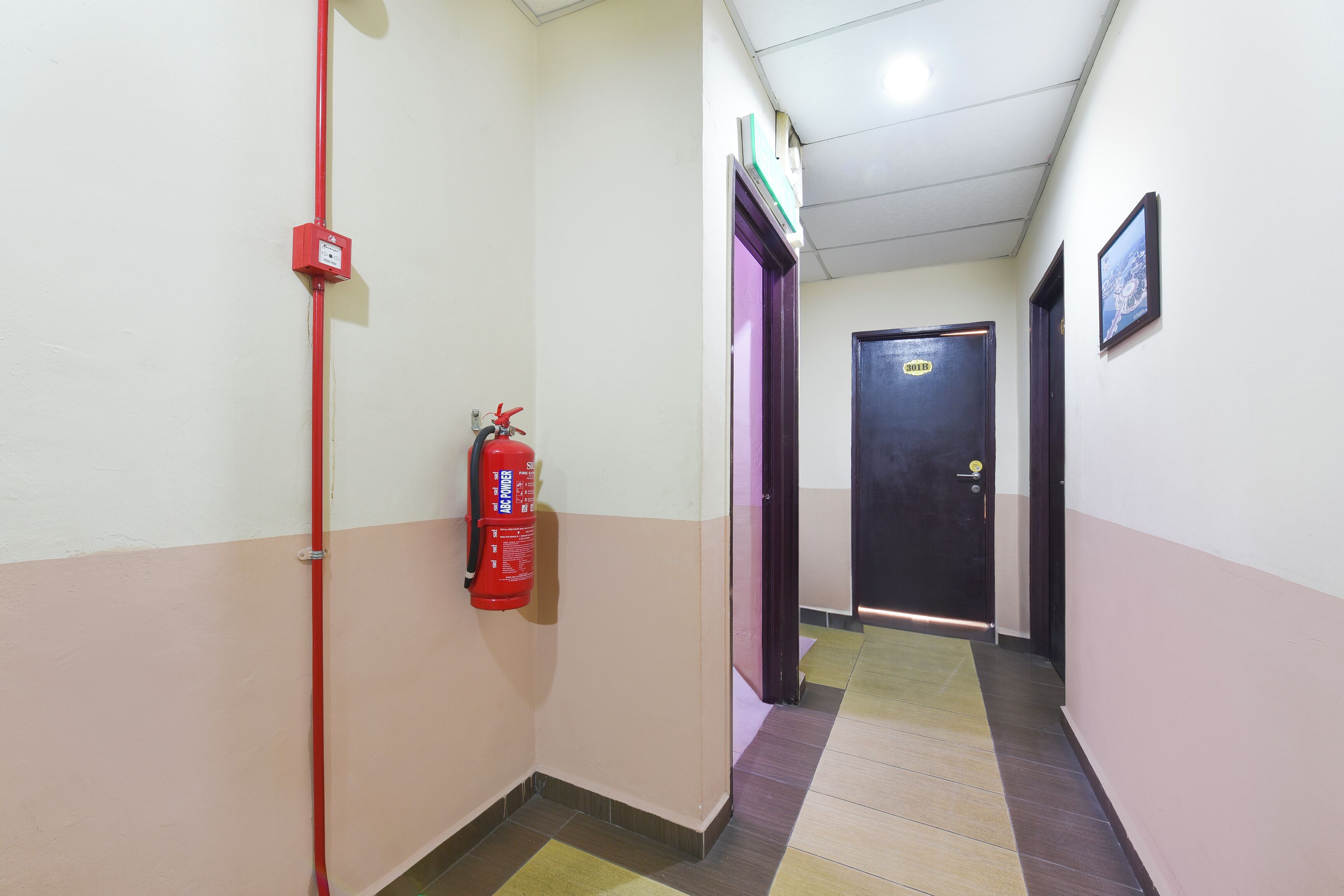 A hallway with a fire extinguisher mounted on the wall, a door at the end, and a tiled floor.