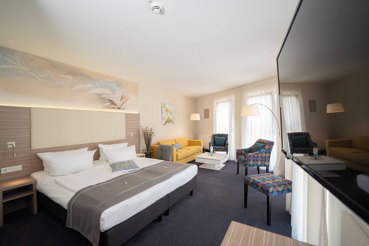 Una habitación de hotel con una cama grande, un sofá, una silla, un escritorio y un espejo.