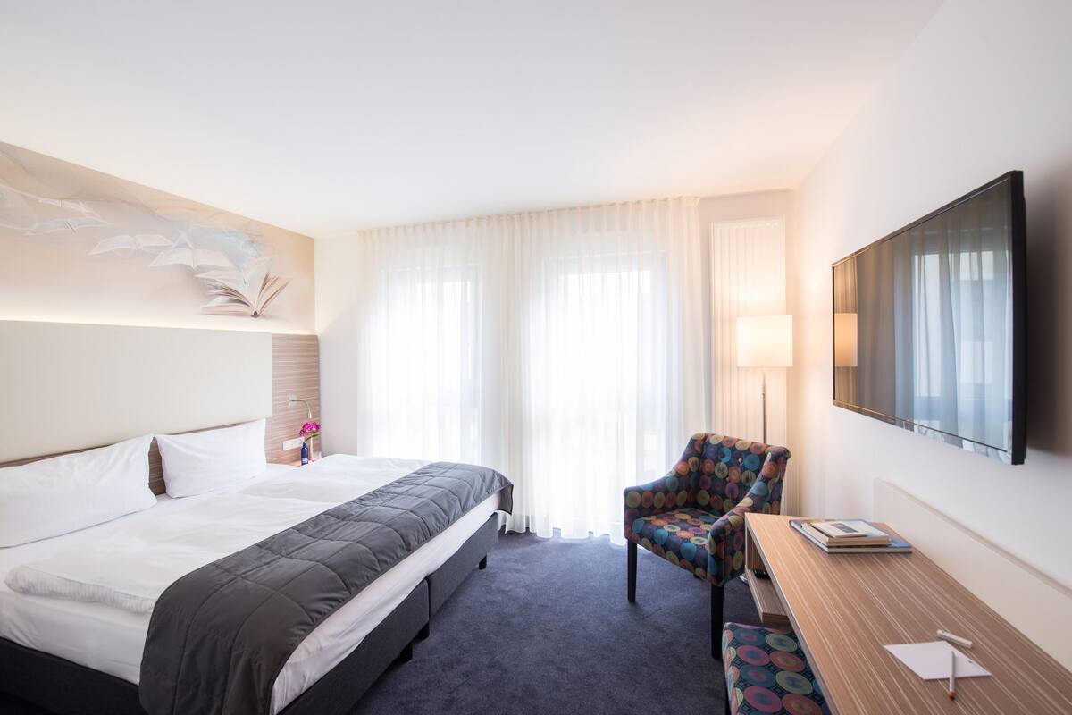 Una habitación de hotel con una cama, una silla, un escritorio y un televisor.