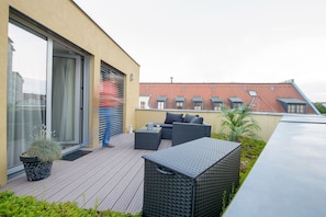 A rooftop patio with outdoor furniture, a potted plant, and a view of neighboring buildings. - Book Hotel Leipzig (Leipzig)