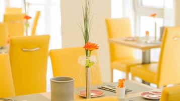 Un comedor con sillas y mesas amarillas, un jarrón con una flor, y un candelabro con velas.