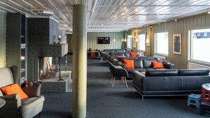 Un vaste espace salon doté de canapés en cuir, d’une cheminée en briques et de grandes fenêtres laissant entrer la lumière naturelle.