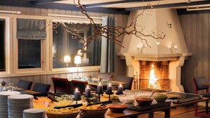 Un coin repas agrémenté d’une cheminée, avec des tables dressées, où l’on a disposé des assiettes, des bols et des bougies.