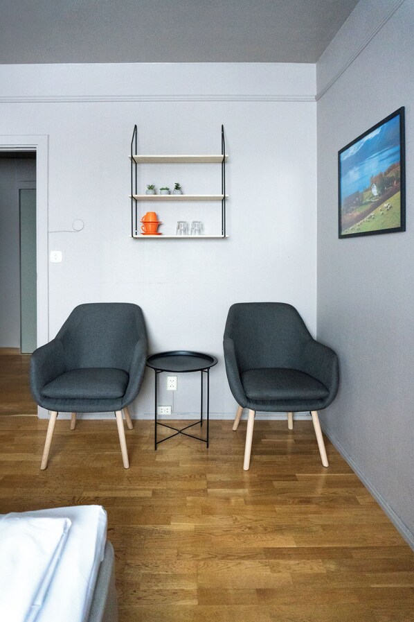 Una habitación con dos sillones grises, una mesita y una estantería con objetos decorativos.