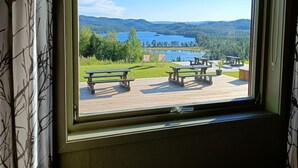 Une fenêtre donnant sur un espace de pique-nique au bord du lac, avec des bancs et, au loin, une chaîne de montagnes.