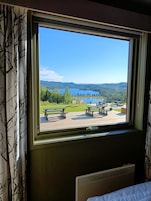 A window with a view of a lakeside picnic area, benches, and a distant mountain range.