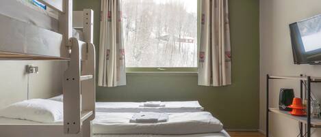 A room with bunk beds, a window with curtains, a television, and a shelf with items.