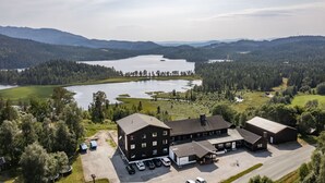 Un chalet doté d’un espace de stationnement, un bâtiment avec de nombreuses fenêtres et une vue sur un lac entouré de collines boisées.