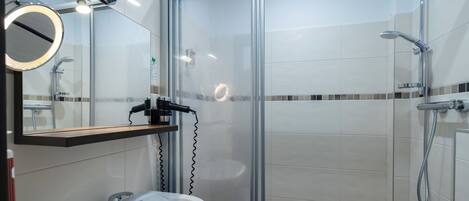 Un baño moderno con ducha envuelta en vidrio, lavamanos y espejo con marco redondo.