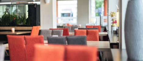 Un restaurante moderno con sillas tapizadas en rojo y gris, un acuario grande y un jarrón con plantas secas.