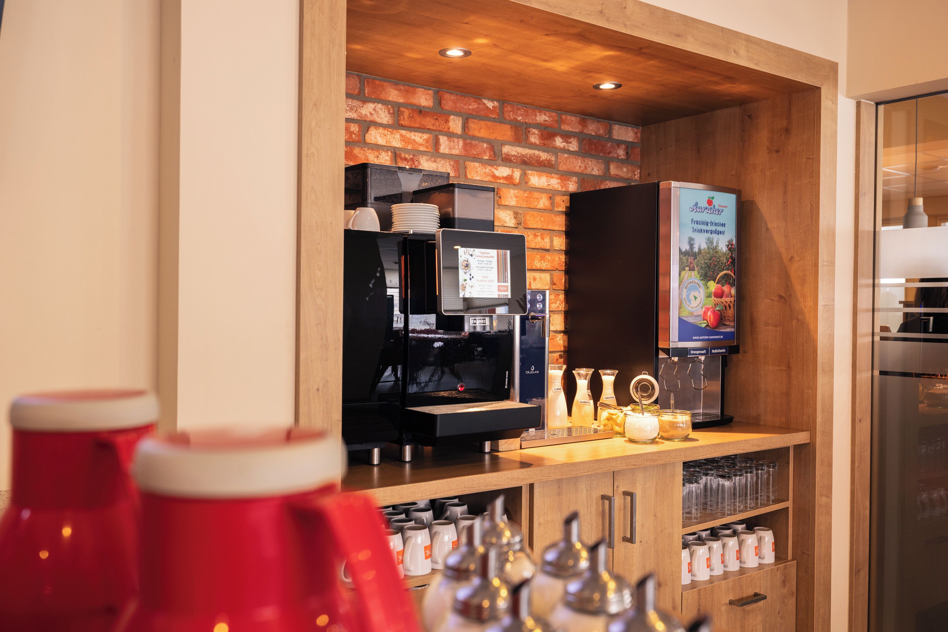 A coffee station with a coffee machine, a display of coffee cups, and a refrigerator.