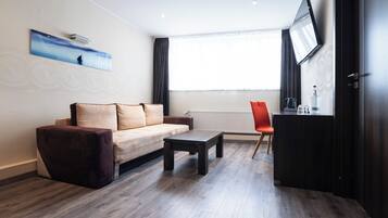 A modern living room with a sofa, a coffee table, a red chair, and a flat-screen TV mounted on the wall.