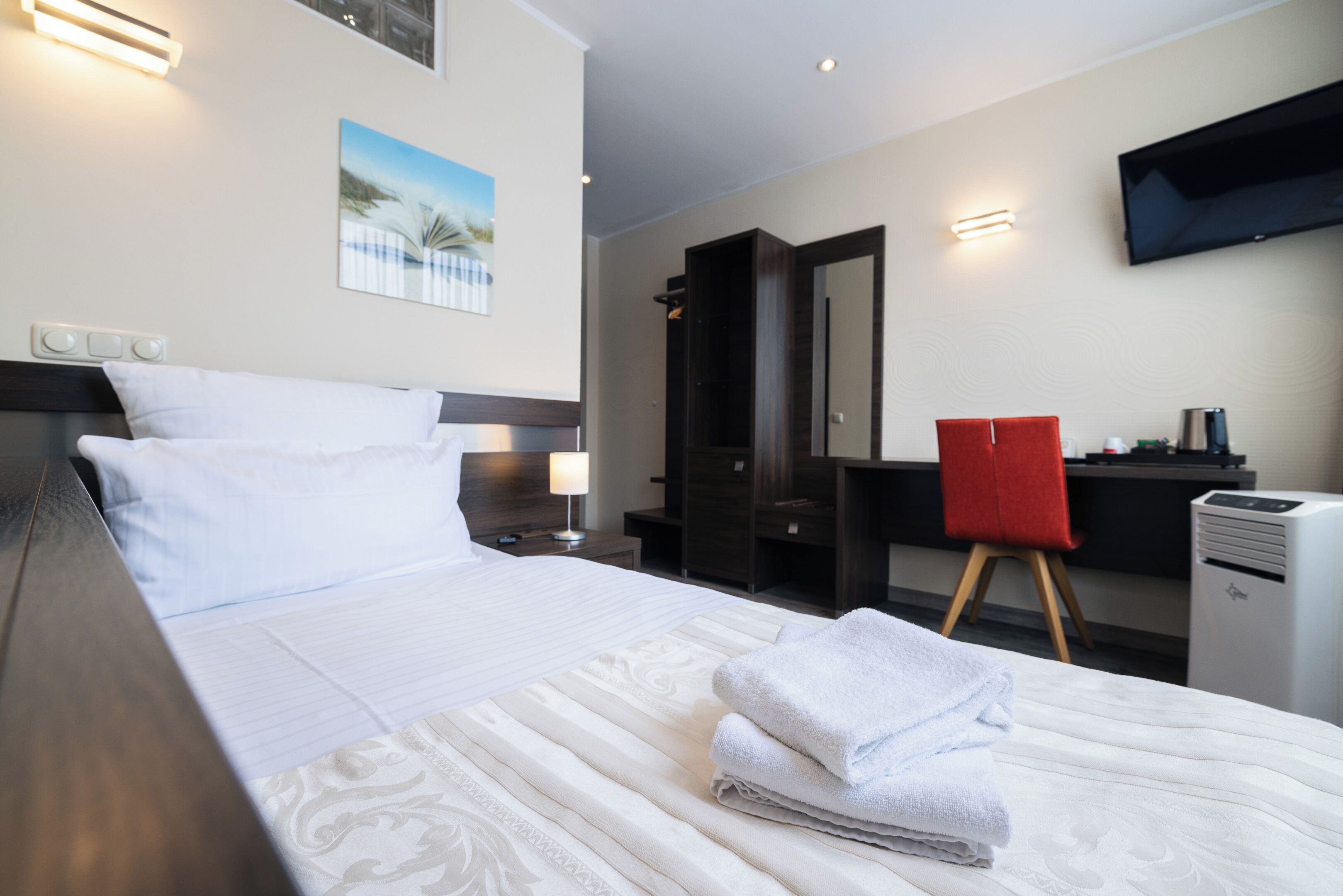 Una habitación de hotel con cama, escritorio, silla, televisor y espejo.