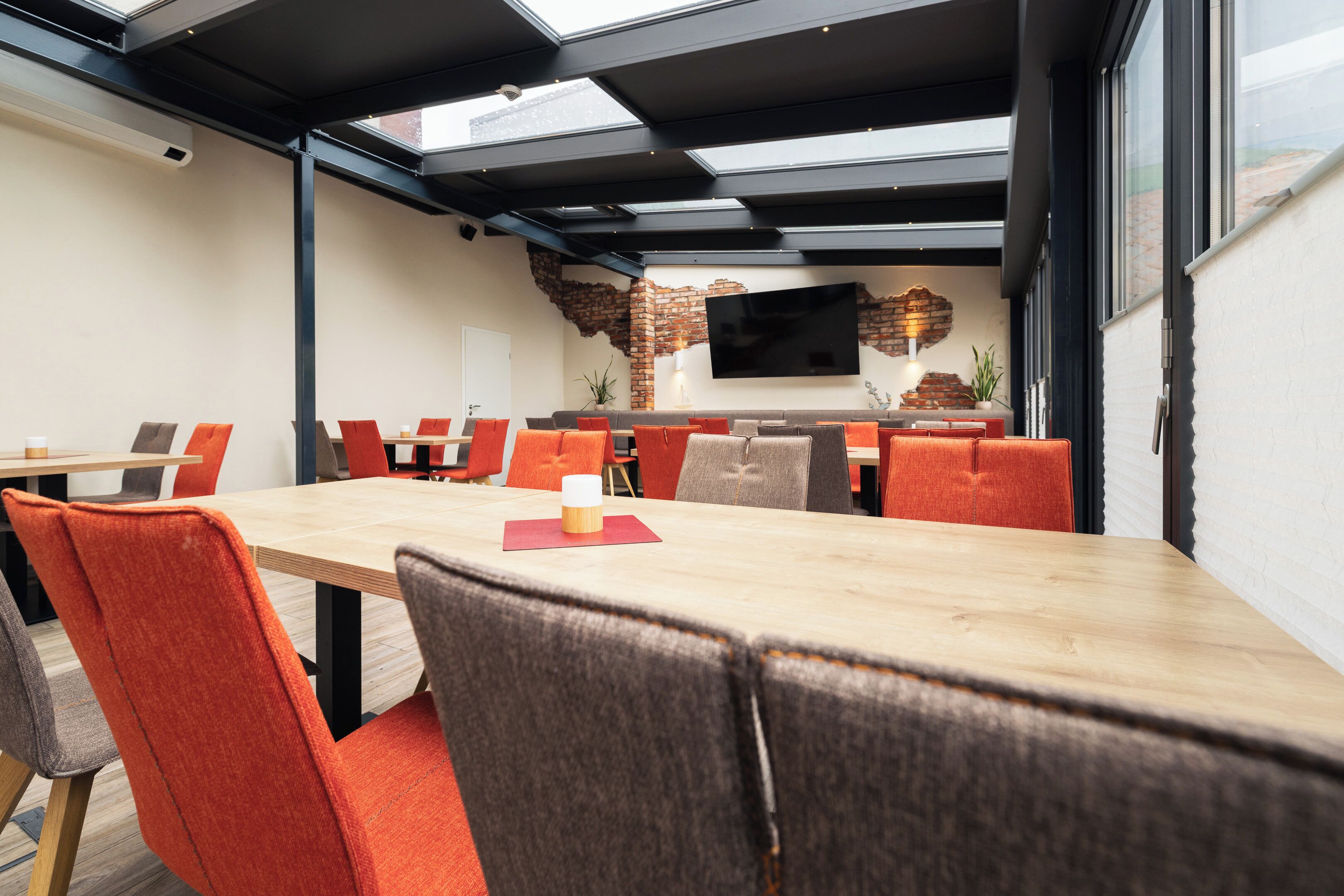 A modern dining area with a long table, orange chairs, and a brick accent wall.