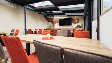 A modern dining area with a long table, orange chairs, and a brick accent wall.