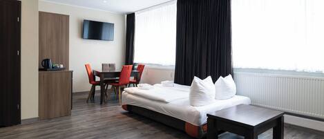 A modern hotel room with a large bed, a desk, and a TV.