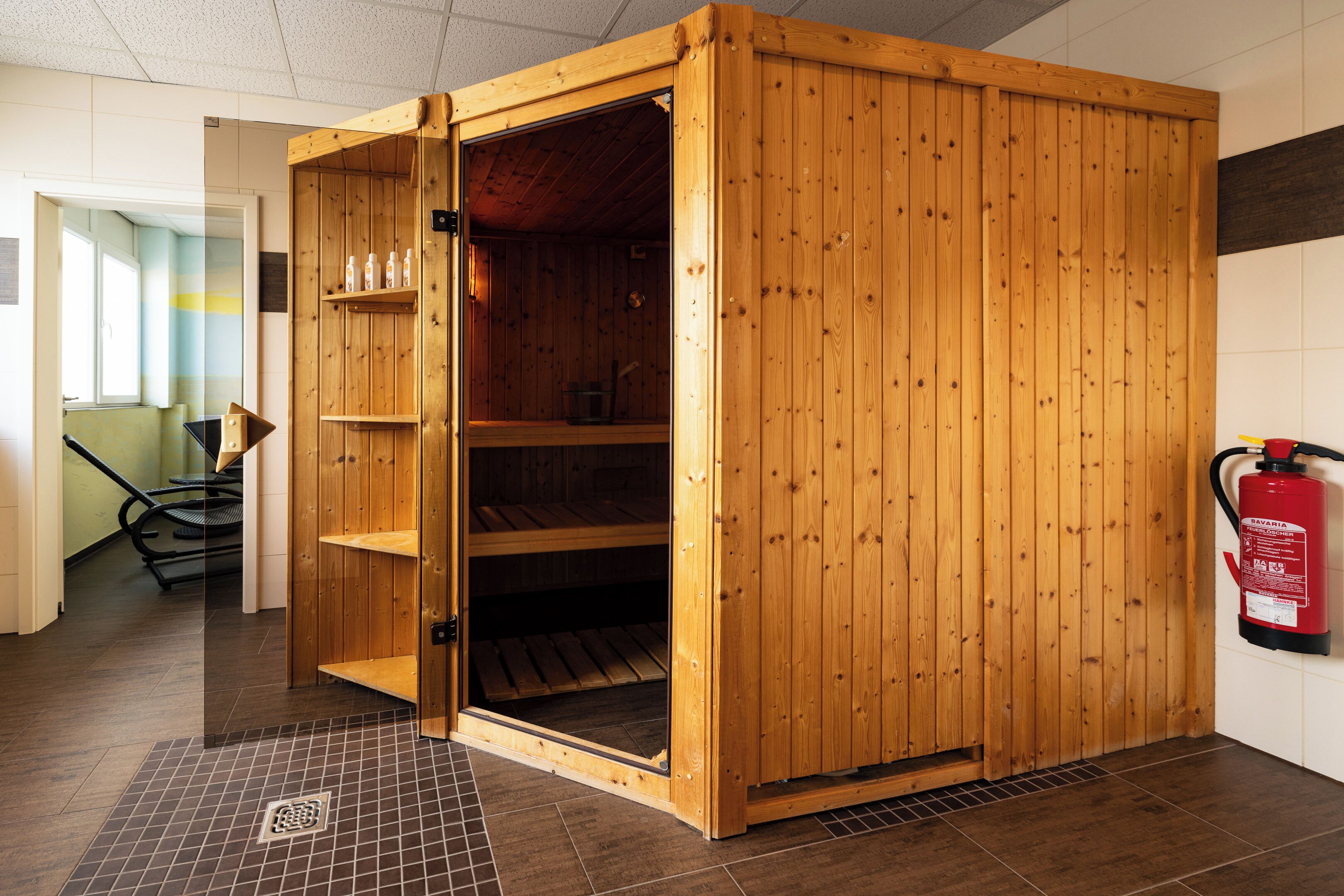 Eine Sauna mit Holzfassade, Glastür und gefliestem Boden.