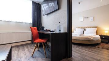 Una habitación de hotel con escritorio, una silla, una cama, televisor y ventana con cortinas.