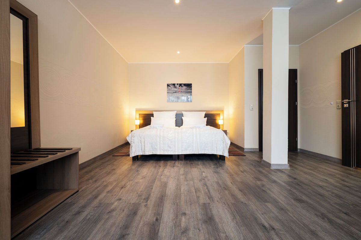 A modern hotel room with a large bed, wooden flooring, and a painting on the wall.