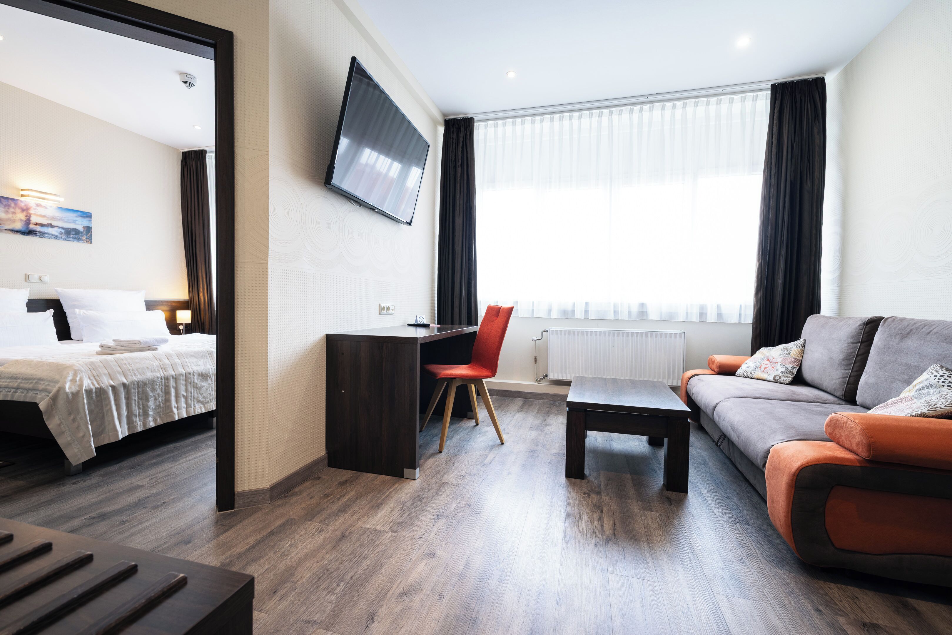 A modern hotel room with a bed, desk, and sofa.