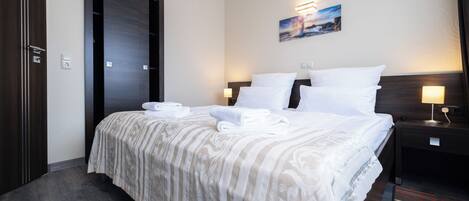 Habitación de hotel con una cama grande, una puerta de madera oscura, un cuadro en la pared y una mesita de noche con lámpara.