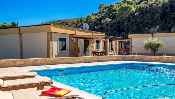 A swimming pool with lounge chairs and a building with a stone facade.