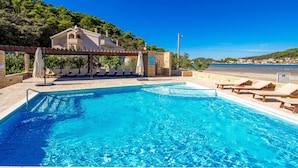 A swimming pool with lounge chairs and a pergola, surrounded by a hillside and a clear blue sky. - Lando Resort (Rab)