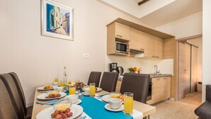 A dining area with a table set for breakfast, a kitchen with wooden cabinets, and a painting on the wall. - Lando Resort (Rab)