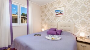 A neatly made bed with a purple bedspread, a tray with a cup and a book, and a framed picture on the wall.