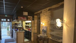 Una zona de bar con una pared de piedra rústica, una barra con caja registradora y estantes con vasos.