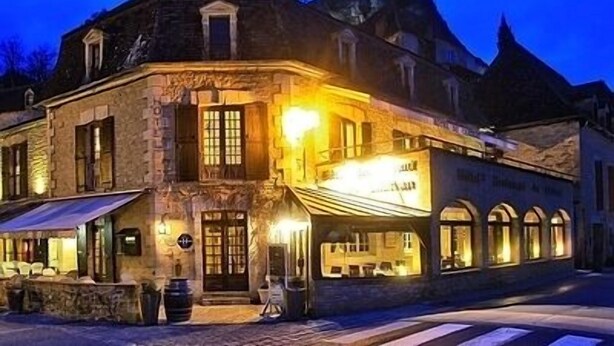 Un edificio histórico con fachada de piedra, ventanas grandes y cálida iluminación interior.