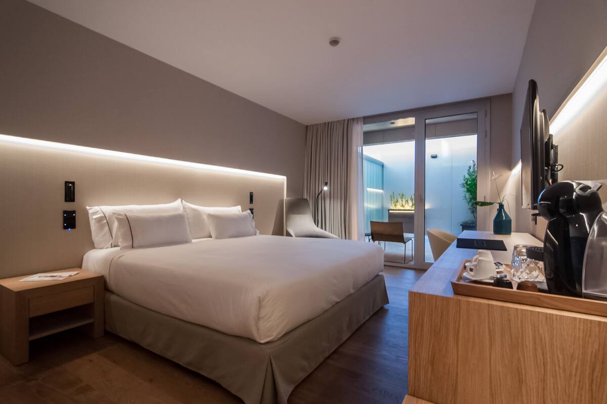 A modern hotel room with a large bed, bedside table, and a desk with a coffee maker.