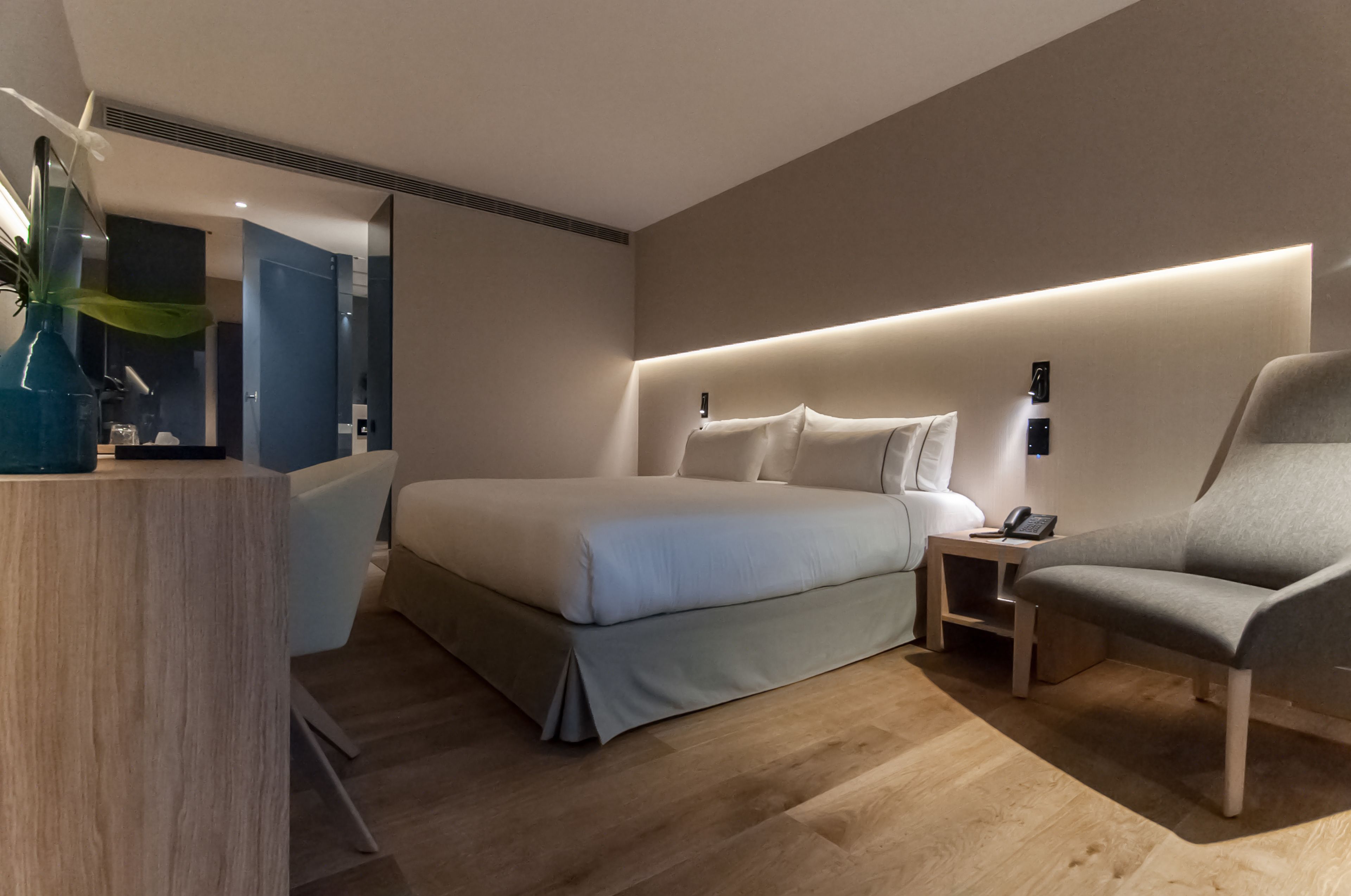 A modern hotel room with a large bed, bedside tables, a seating area, and a plant.